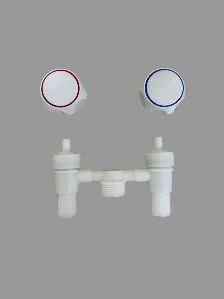 White plastic dual-handle valve trim set with two white hexagonal knobs, one featuring a red ring and the other a blue ring, positioned above a matching horizontal cross-connecting pipe assembly on a speckled beige stone surface.